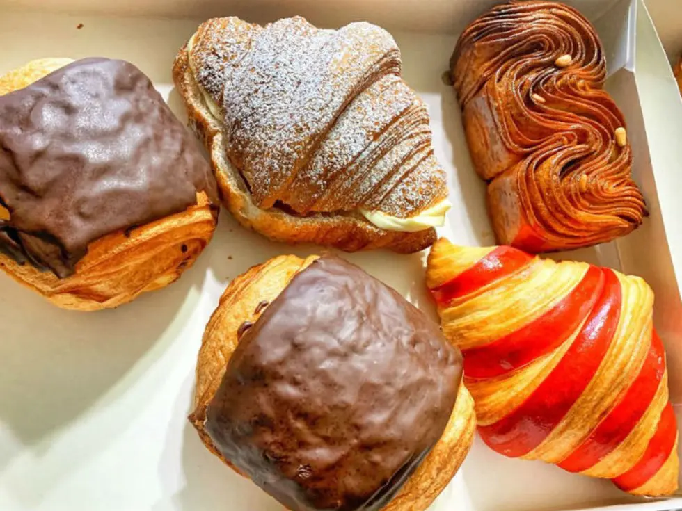 Assorted pastries including chocolate-glazed puffs, powdered croissant, spiral pastry, and red-and-yellow striped eclair in a white box