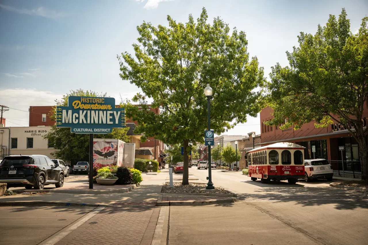 Historical Downtown McKinney welcome sign and red and white trolly on street