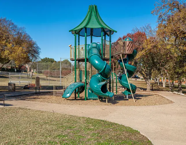 Teal and green playground structure with twin spiral slides and climbing features in a park setting with bare autumn trees