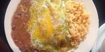 Plated Mexican food with refried beans, shredded cheese, rice, and what appears to be meat on a white dish