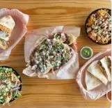 Overhead view of Mexican street tacos and sides on wooden table with pink paper wrapping