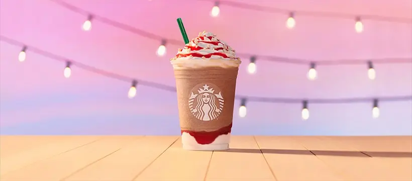 Iced coffee drink with whipped cream and sprinkles, string lights glowing in pink-toned background