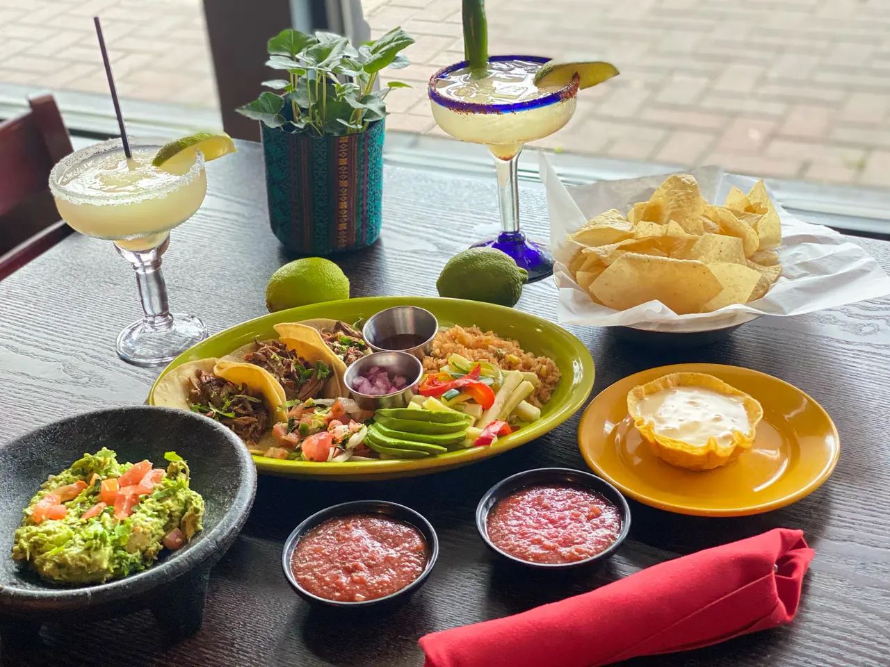 Table spread with fajitas, guacamole, cured meats, chips, and margarita cocktails with lime garnish