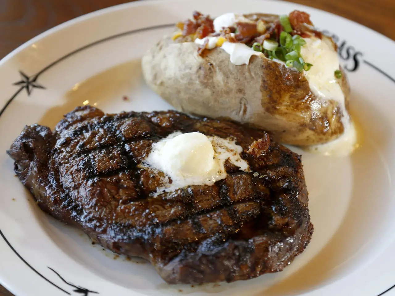 Grilled steak with melting butter and a loaded baked potato topped with sour cream and bacon