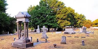 Historic cemetery with stone monuments and markers scattered across grassy grounds beneath mature trees