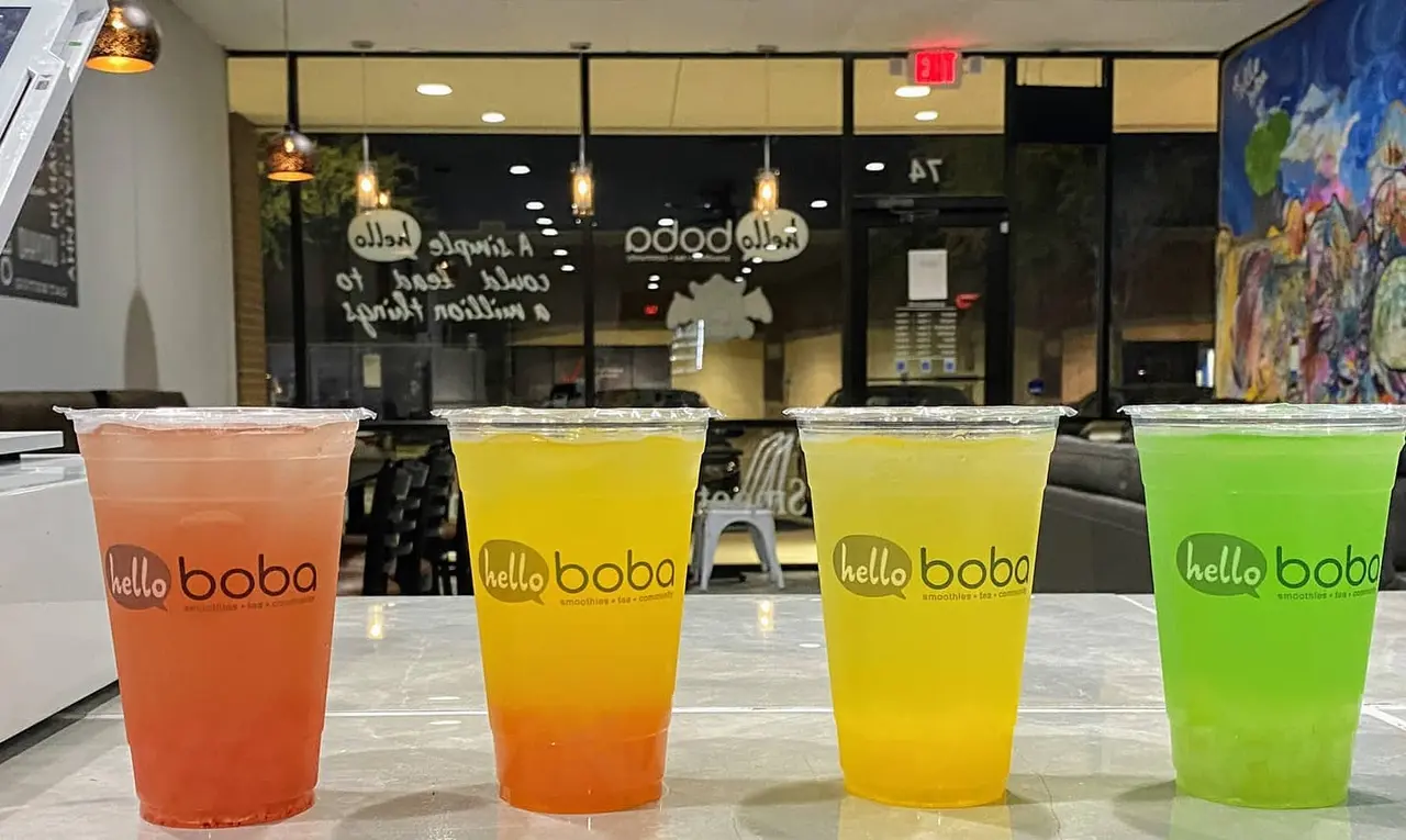 Four colorful bubble tea drinks in clear cups lined up in front of the storefront, ranging from coral red to bright green