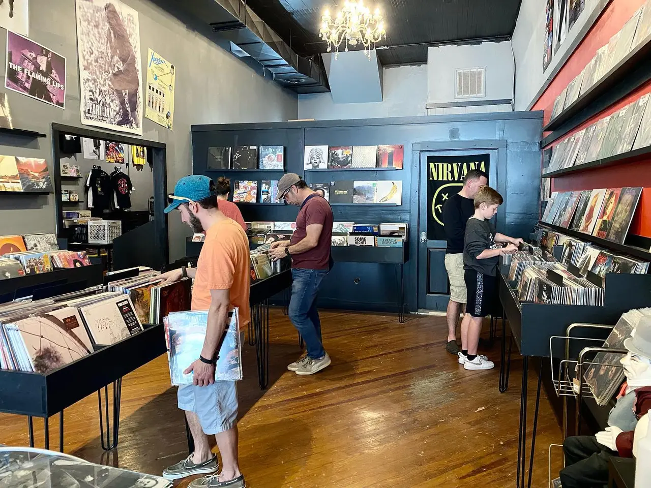 Customers browsing vinyl records and music merchandise in a record store with blue walls and wooden floors