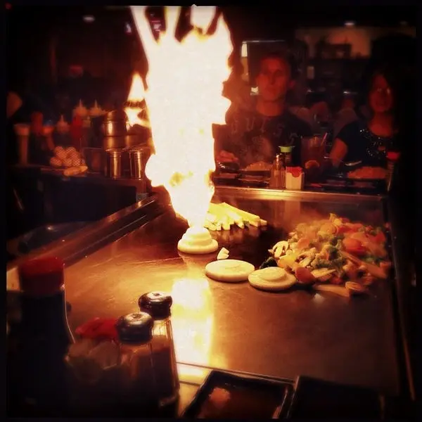 Chef performing flaming teppanyaki cooking at hibachi counter with seated diners watching