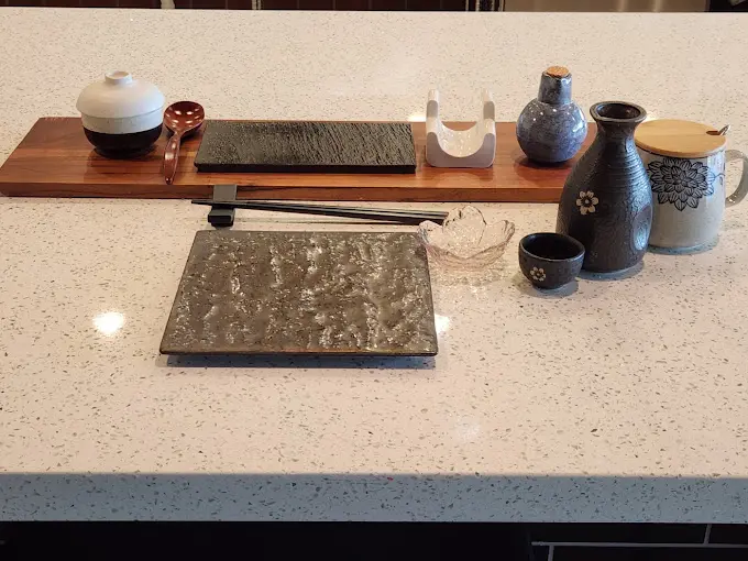 Japanese ceramic vessels, chopsticks, and serving pieces arranged on wooden and stone surfaces