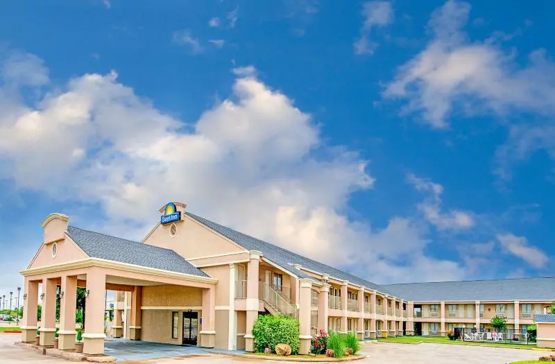 Tan single-story hotel building with covered entrance portico under blue sky with white clouds