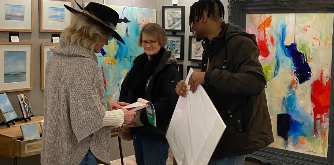 three people and one is selling a painting that is on the wall
