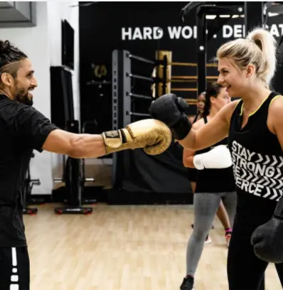 Male trainer in black gloves guiding female boxer's punch technique during training session in gym
