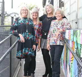 four ladies standing on a walkway leaning on a handrail