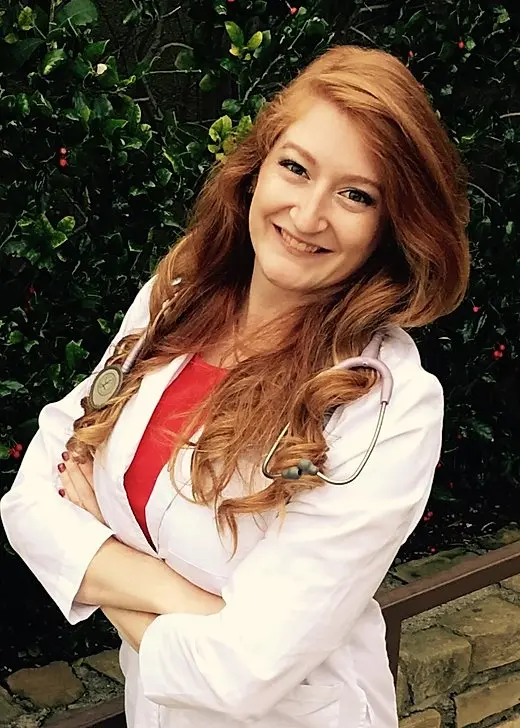 Healthcare professional in white coat and stethoscope smiling in front of green foliage