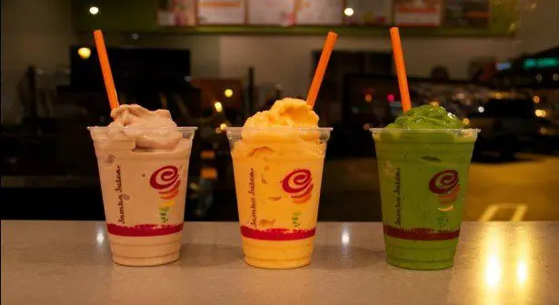 Three colorful smoothie drinks with straws in clear cups on a counter, featuring cream, orange, and green beverages