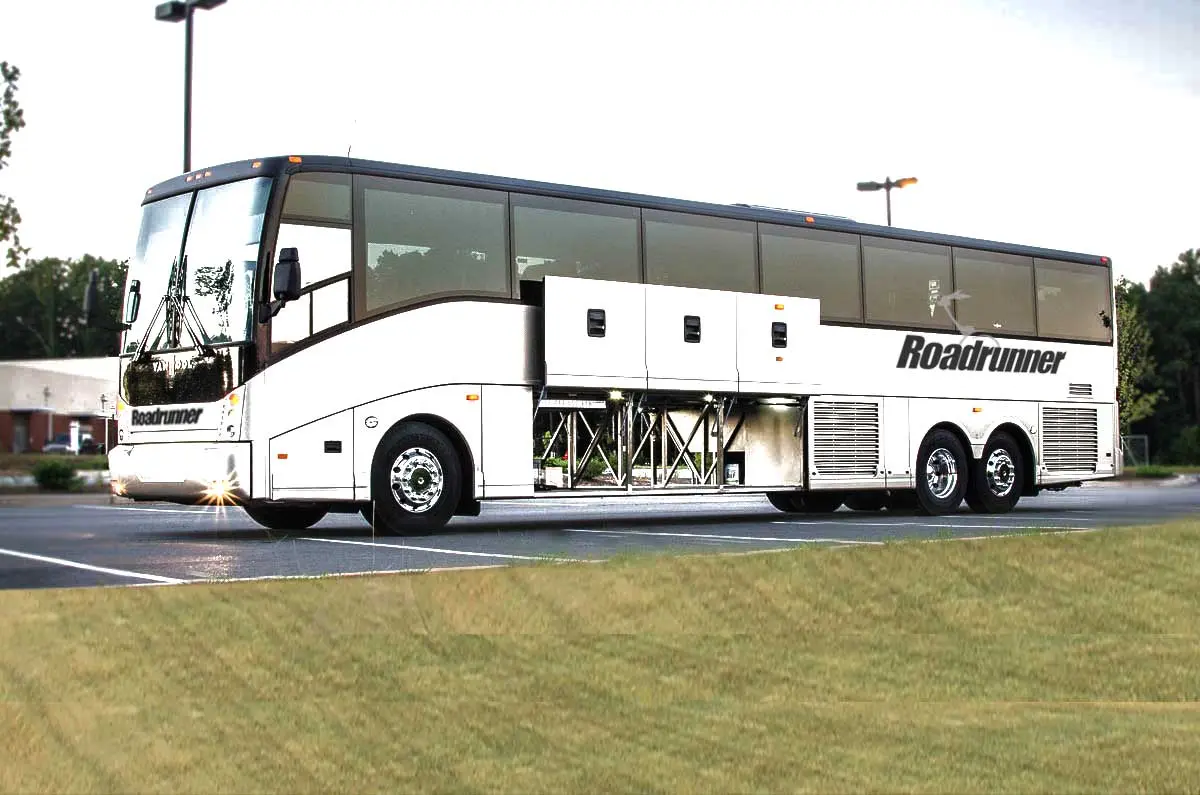 White and gray double-decker motorcoach parked on grass with trees in background