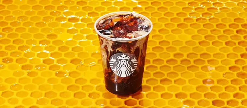 Cold dark beverage in clear cup with lid against yellow honeycomb background