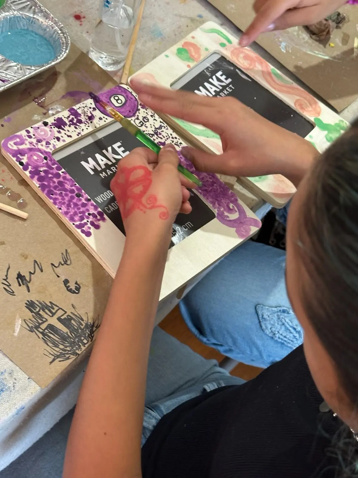 Child decorating a picture frame with purple sequins and glitter during an art activity
