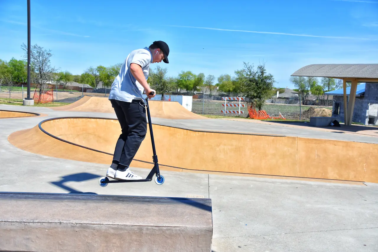 Person riding a scooter in a skate park with curved wooden ramps and clear blue sky