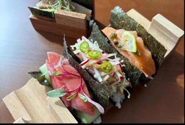 Assorted sushi hand rolls and nigiri sushi arranged on wooden serving boards with fresh garnishes and nori seaweed