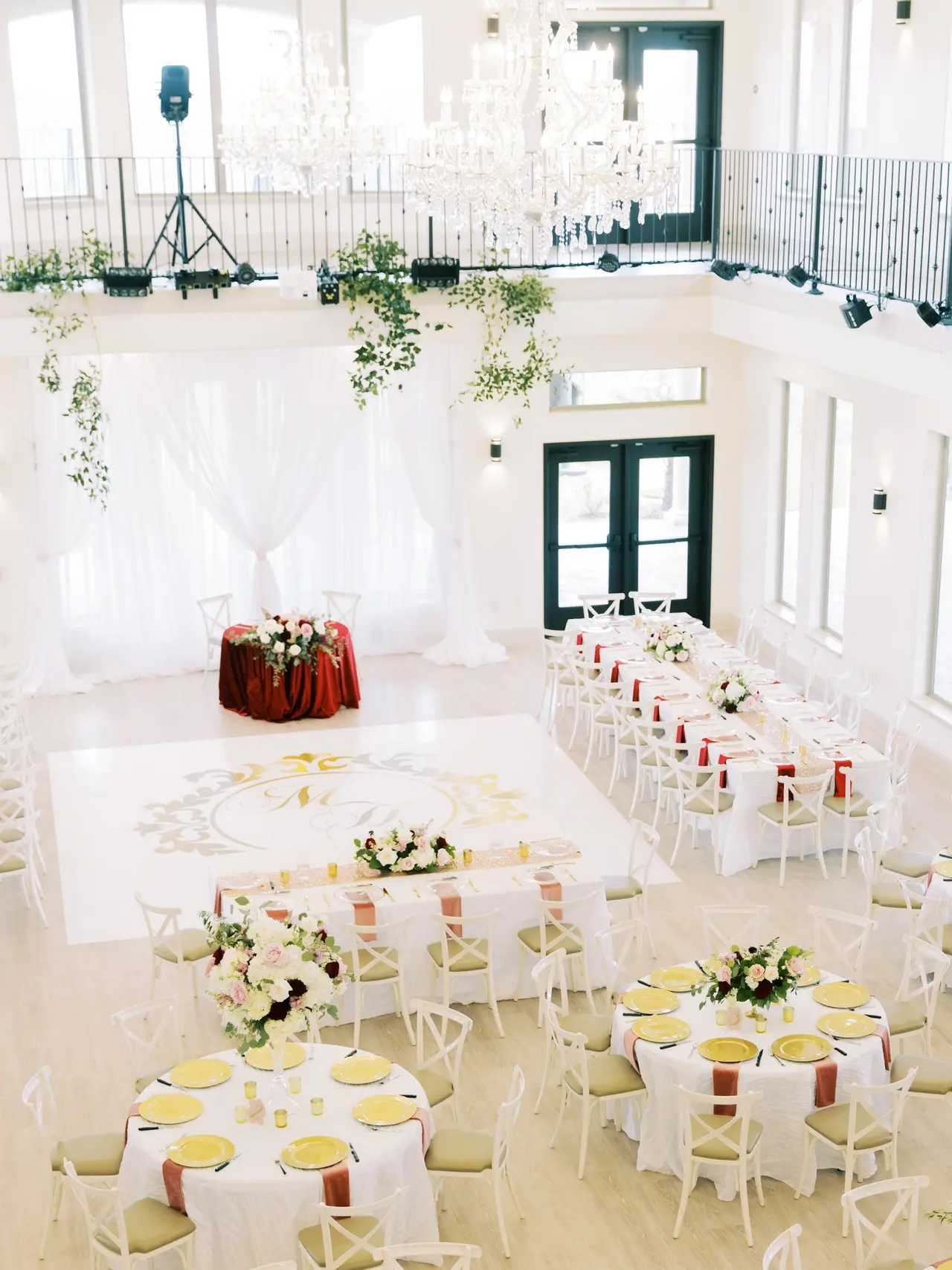 Bright event space with round tables set for dining, white chairs, floral centerpieces, and cascading greenery from upper level railings
