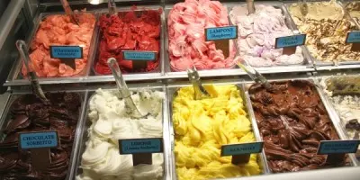 Display case with multiple flavors of gelato in various colors including pink, red, white, yellow, and brown