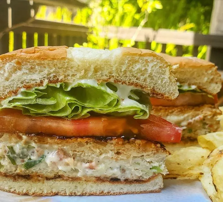 Toasted sandwich with lettuce, tomato, and spread filling, served with french fries on outdoor patio
