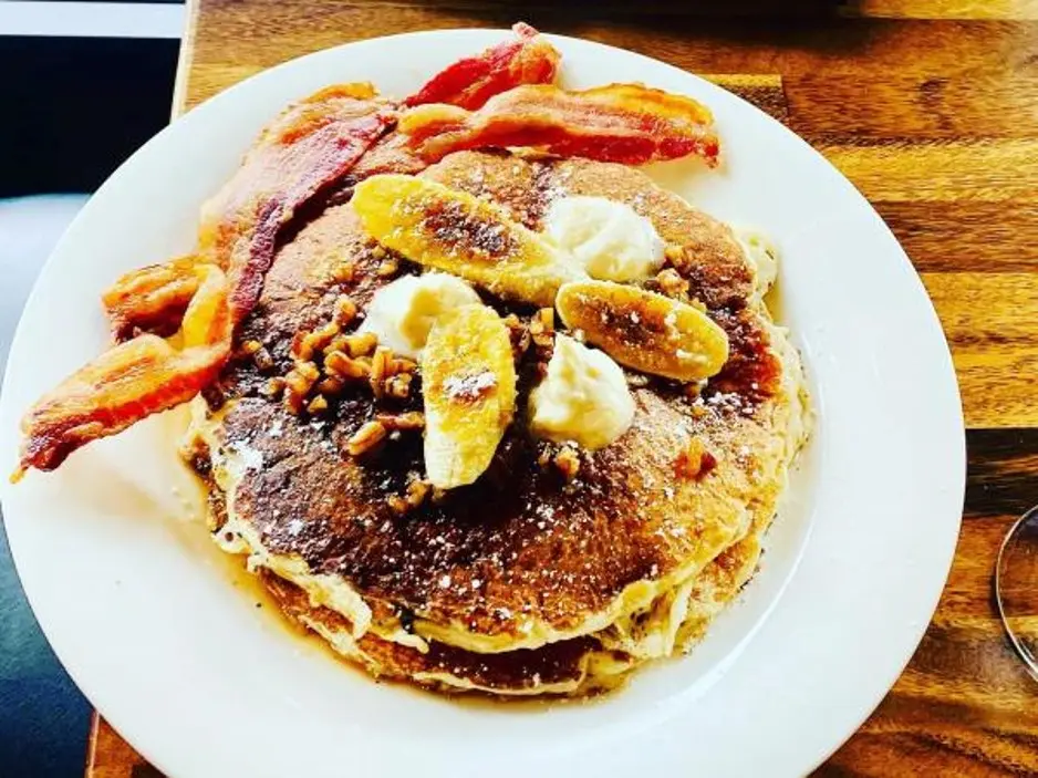 Sweet pancakes with bananas and nuts on top and crispy bacon on the side