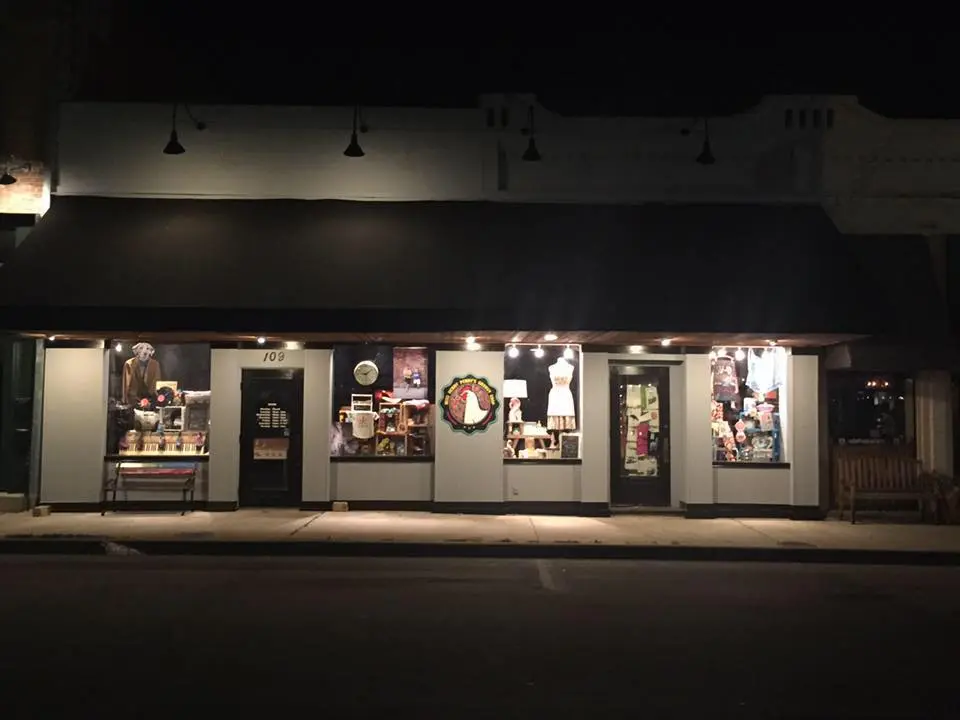 Illuminated storefront display windows at night featuring vintage and eclectic merchandise arranged across multiple sections