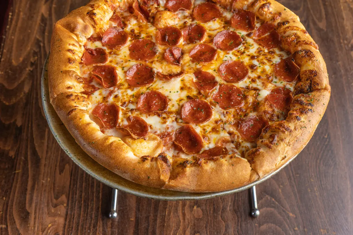 Pepperoni pizza with golden crust on a wire stand against a dark wood surface