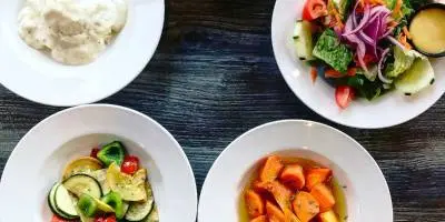 Four white plates with grilled vegetables including zucchini, carrots, and salad on dark wooden table