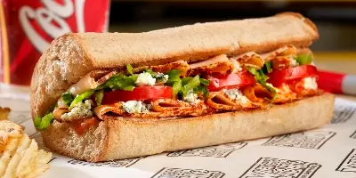 Pulled pork sandwich with lettuce, tomatoes, and white cheese on crusty bread, served with french fries