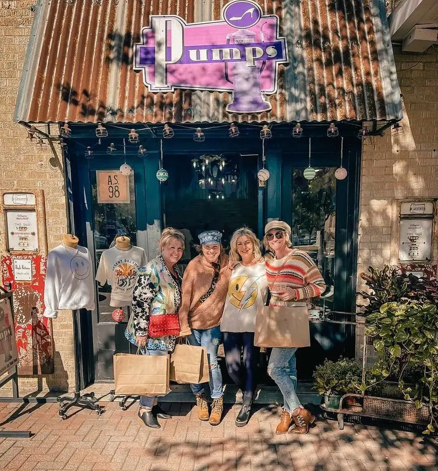 Four people standing outside a storefront with pink and purple signage and dark blue door, holding shopping bags