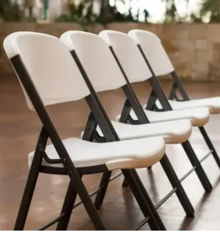 Row of white folding chairs with black frames on outdoor ground