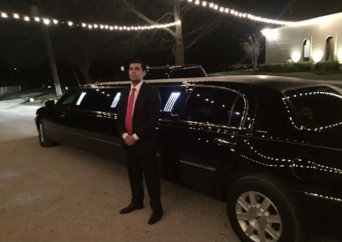 Man in suit standing beside black limousine decorated with white lights at night