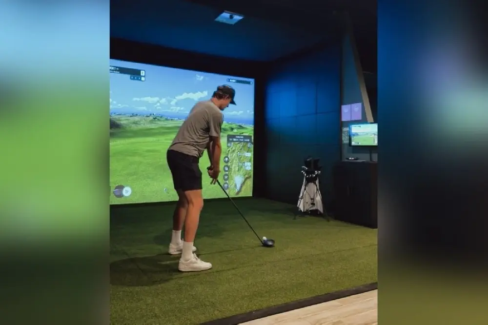Golfer practicing swing on indoor golf simulator with large screen displaying virtual course landscape