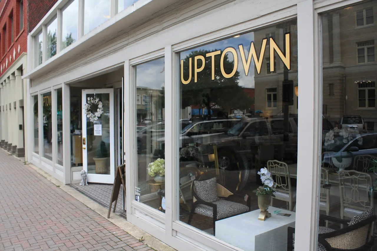 Storefront with large windows displaying home furnishings and decor, yellow "UPTOWN" signage visible on glass