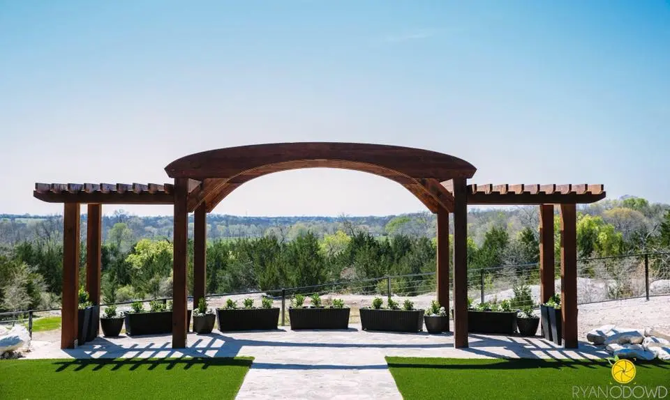 Wooden pergola structure with benches overlooking landscaped grounds and forested hills under clear sky