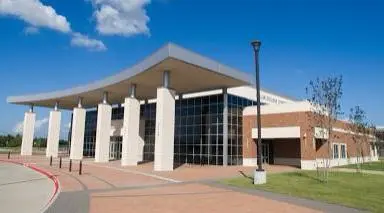 Modern brick and white building with large windows and covered entrance, set on manicured grounds under blue sky