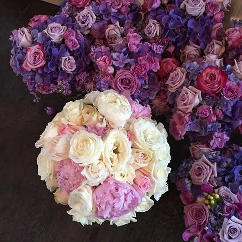 Overhead view of white and pink rose bridal bouquet surrounded by purple and pink floral arrangements on dark surface