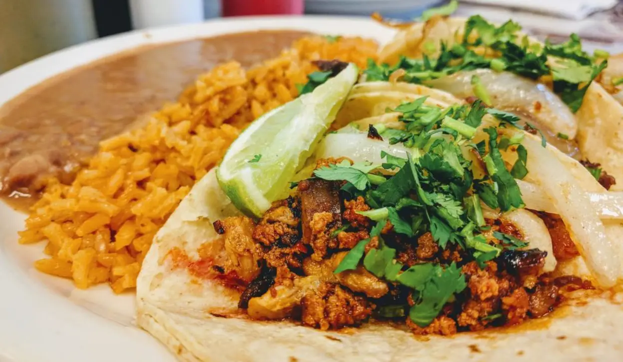 Soft tacos filled with seasoned meat, topped with cilantro and sliced avocado, served with Spanish rice