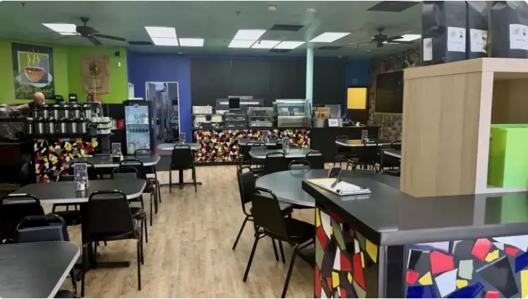 Interior of a casual coffeehouse with colorful walls, tables and chairs, counter seating, and bright lighting throughout the space