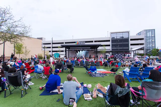 People sitting on lawn chairs watching a concert on an outside stage