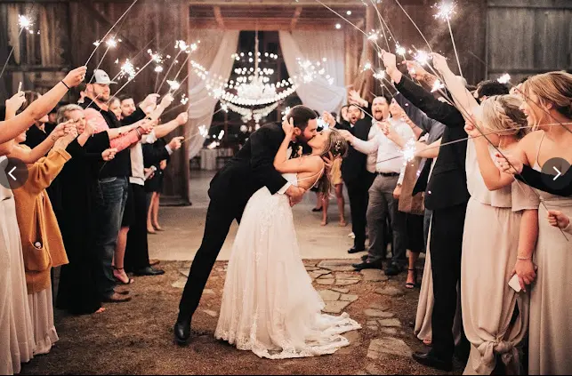 Bride and groom kissing under sparkling lights strung between two lines of guests holding sparklers