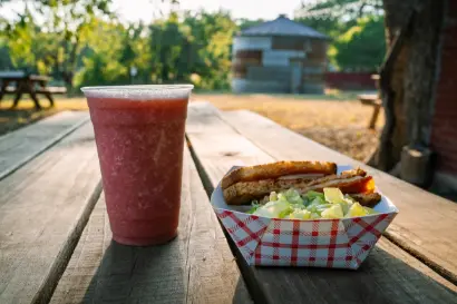 Red smoothie and hot dog with lettuce in checkered paper basket on wooden picnic table outdoors