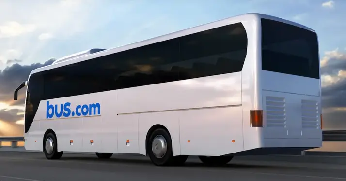 White coach bus with blue "bus.com" text on side, parked against cloudy sky