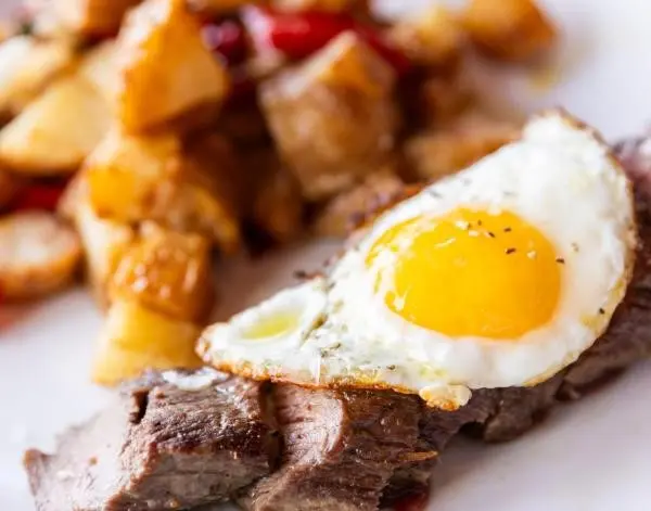 Fried egg places on steak tips with hashbrown potatoes in the background