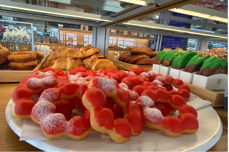 Red sugar-coated pastries and croissants on white plates in a bakery display case with pastries visible in background
