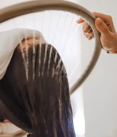Person holding a round mirror, viewing their long dark hair from behind