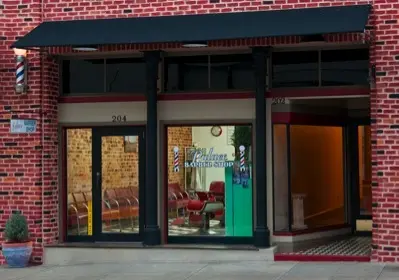 Red brick storefront with dark awning and large windows displaying barber shop interior with vintage decor and seating